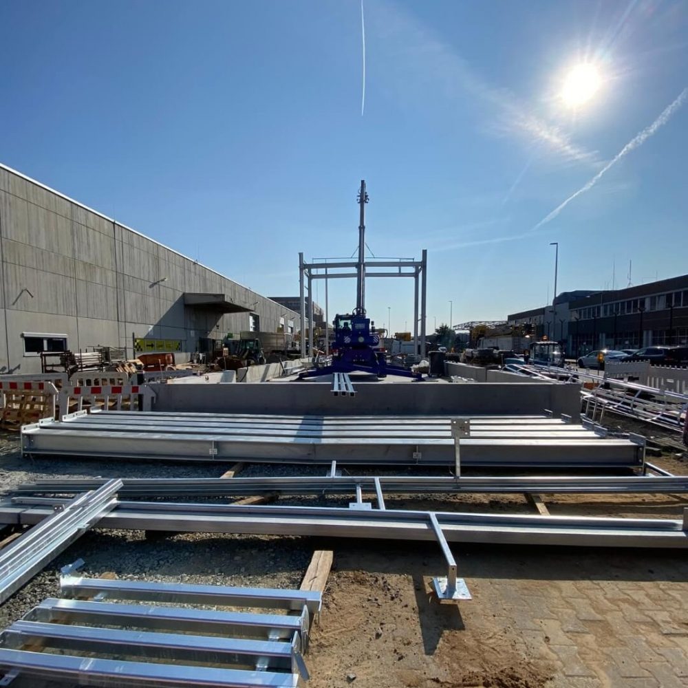 Baustelle Reifenlager mit Stahlträgern, Kran und fertiger Bodenplatte unter sonnigem Himmel – Fortschritt im Bauprojekt Gebäude 100