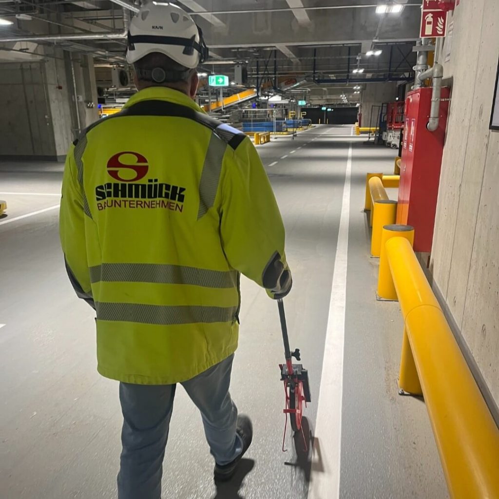 SCHMÜCK-Mitarbeiter führt Einmessarbeiten für die Bodenmarkierungen in der Gepäckförderanlage im Terminal 3 durch.